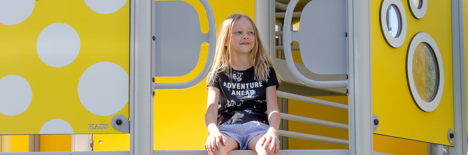 A girl sits on the edge of a playground unit with yellow HPL panels.